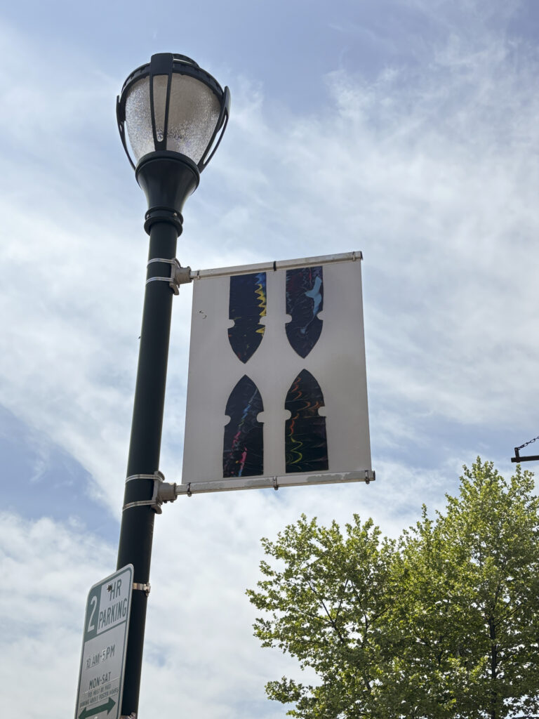 rectangular banner on a light post against a cloudy sky. A tree is visible in the lower right hand corner.