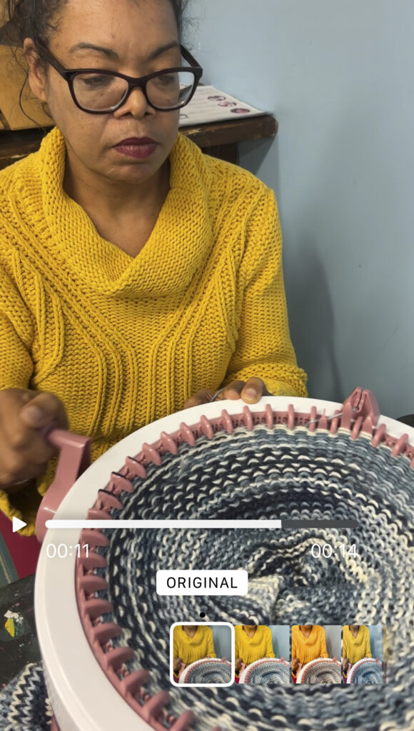 a woman in a yellow sweater using a round knitting machine to make a hat.