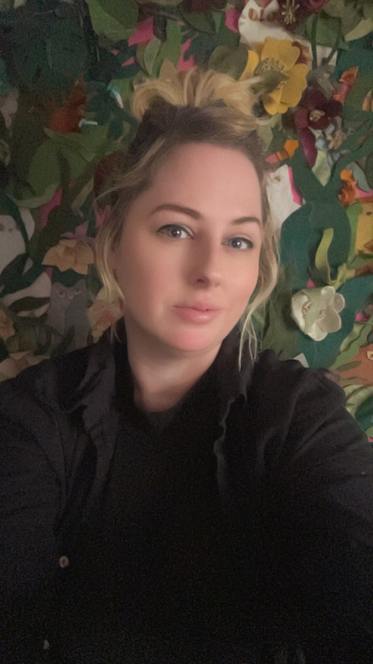 a woman with blond and dark hair with a fabric flower background